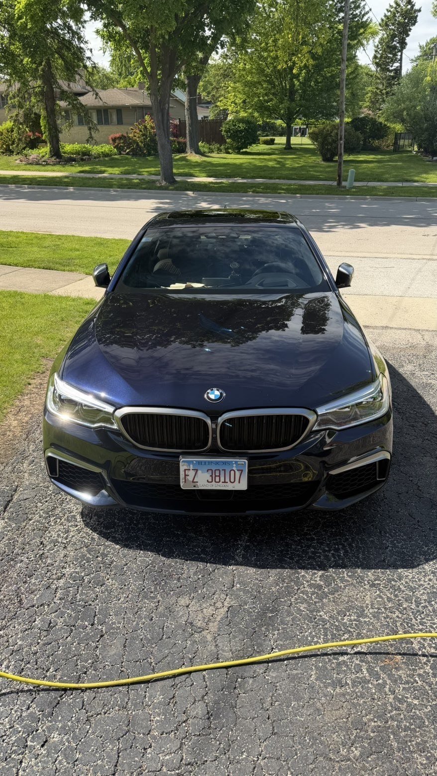 Black BMW sedan parked on a driveway in a suburban neighborhood on a sunny day