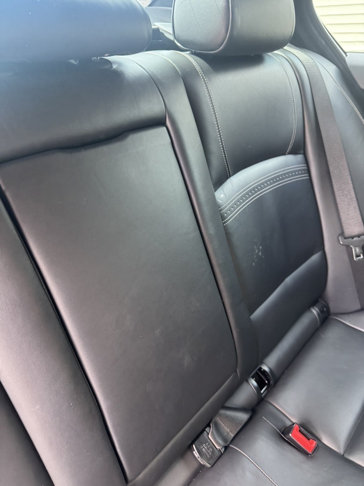 Before: stained and dusty black leather back seat with visible marks on the seat and headrest
